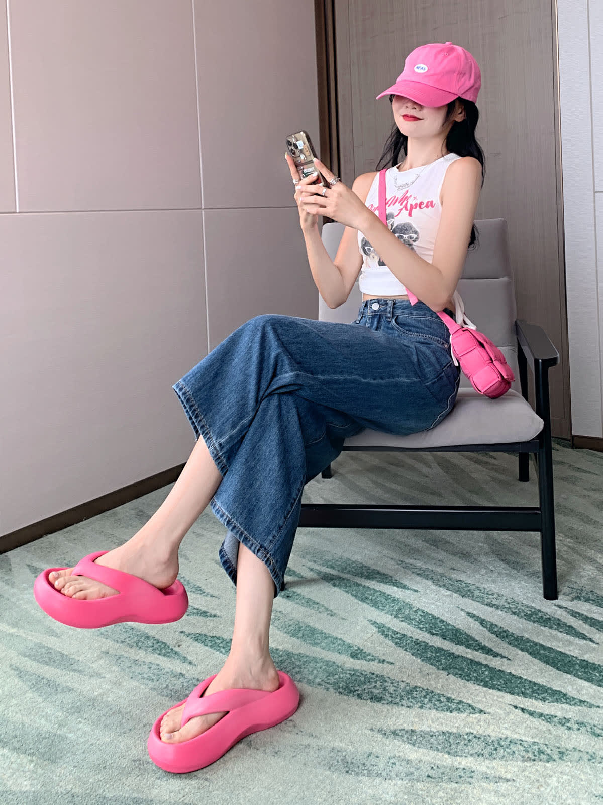 YEEYEEWang 빈티지 블루 와이드레그 진, 아시안핏, 측면으로 의자에 앉아 양손으로 폰을 들고, 핑크 캡과 플랫폼 샌들.