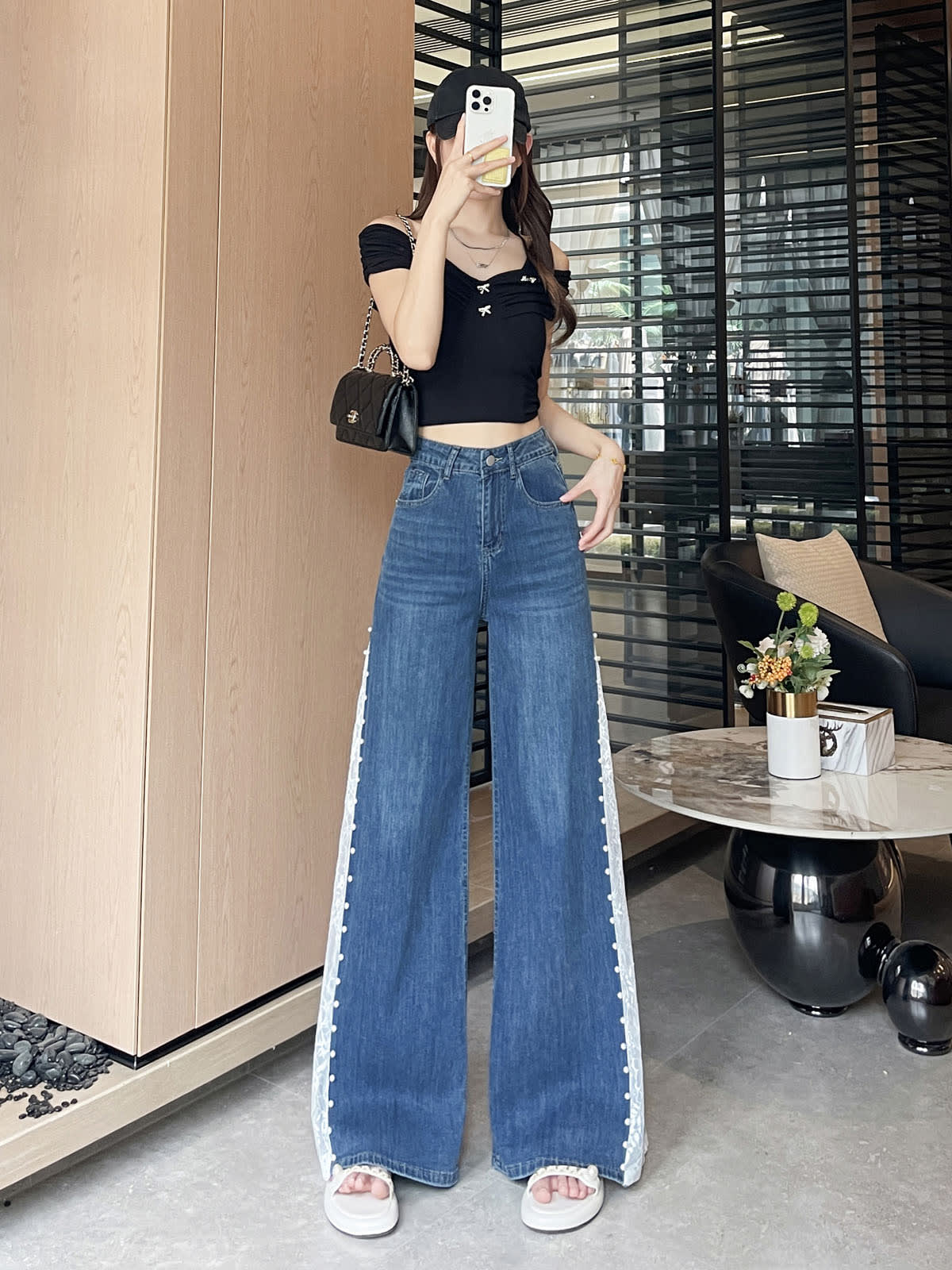 YEEYEEWang 빈티지 블루 와이드레그 진, 아시안핏, 전신 정면 포즈, 얼굴 앞에 휴대폰, 블랙 오프숄더 탑과 체인 백.