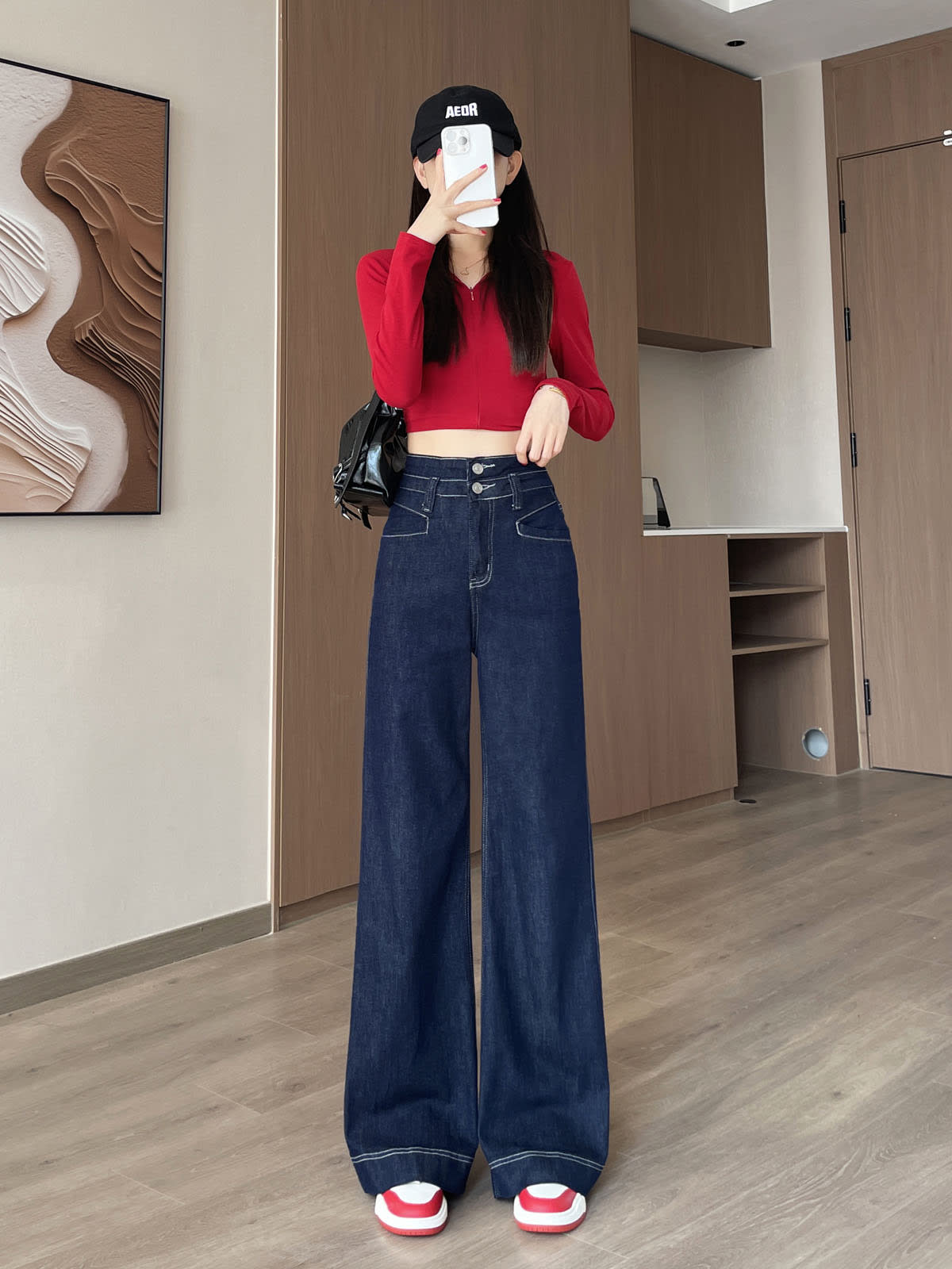 YEEYEEWang 데님 블루 와이드레그 진, 아시안핏, 전신 정면 포즈, 얼굴 앞에 폰, 블랙 캡과 블랙 백.