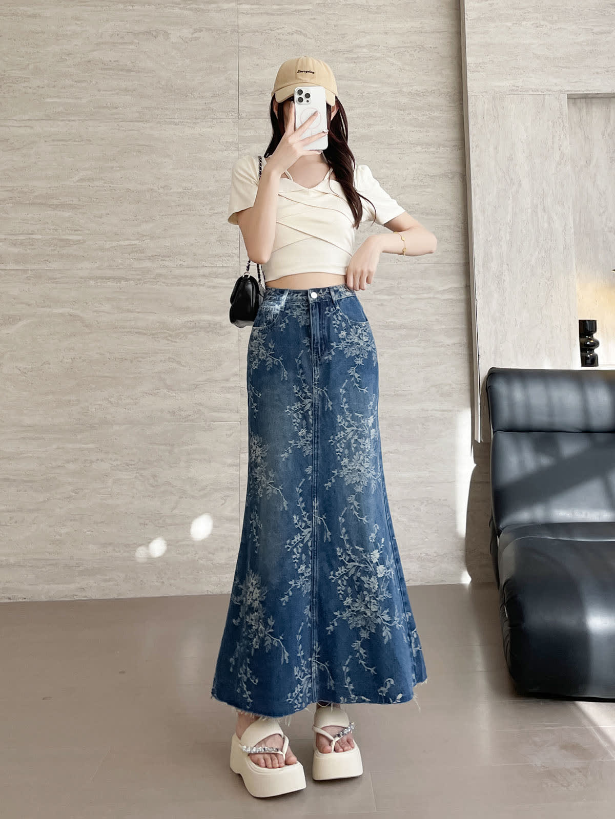 YEEYEEWang 블루 데님 맥시 스커트, 아시안핏, 정면 전신, 휴대폰을 얼굴 앞에 든 서 있는 포즈, 손을 허리밴드에 올림, 베이지 캡과 블랙 체인 백.