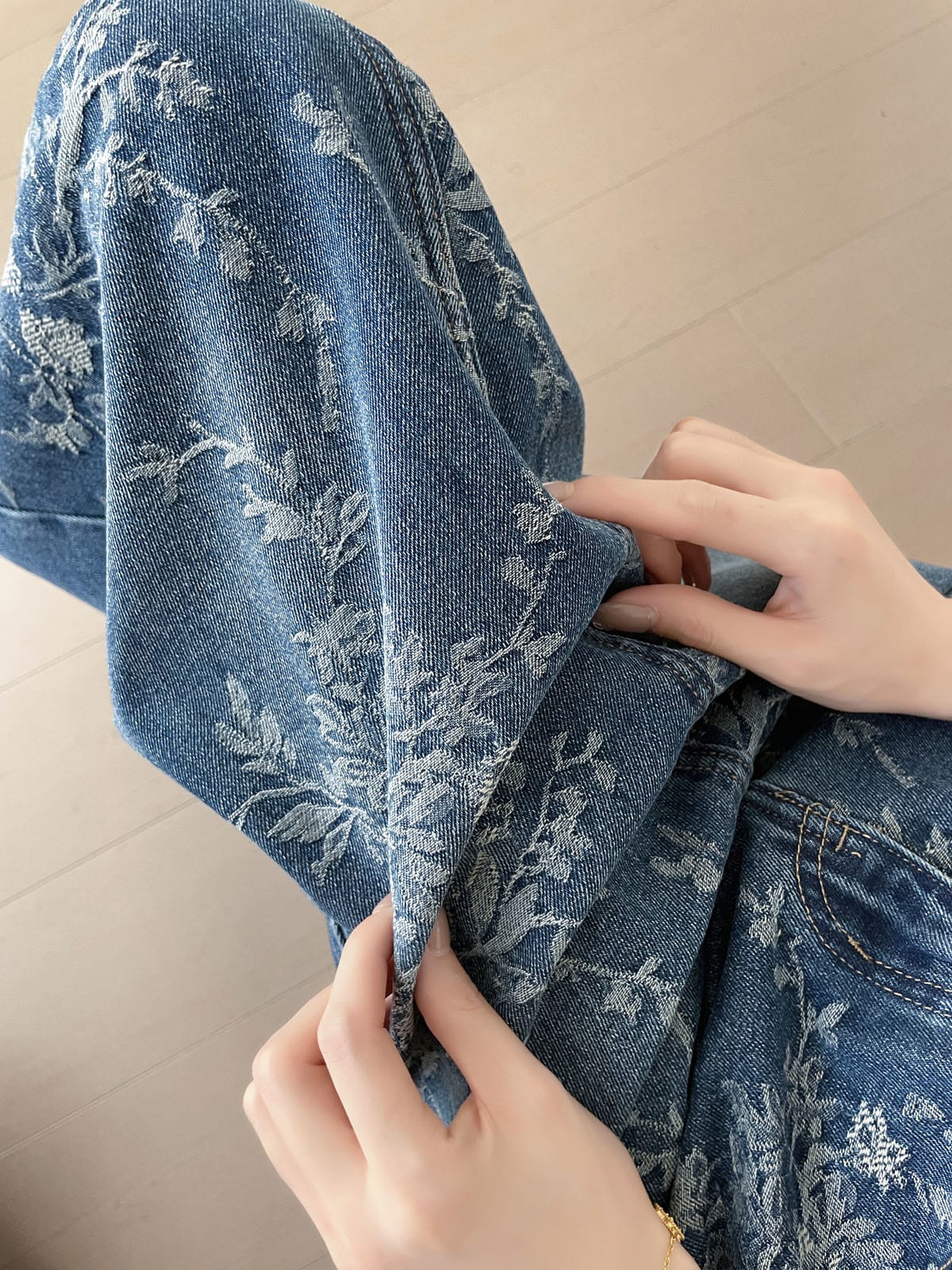YEEYEEWang 블루 데님 맥시 스커트, 아시안핏, 플로럴 자카드 데님 텍스처 클로즈업, 손으로 원단 가장자리를 들어 조직감을 보여주는 모습.