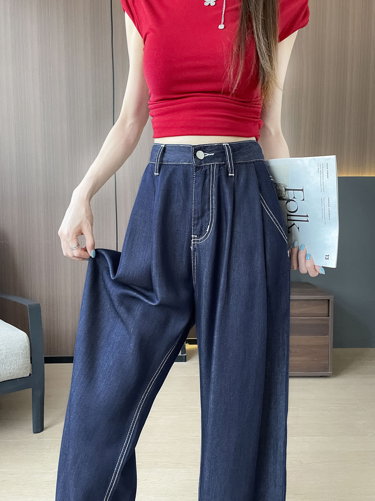 YEEYEEWang 데님 블루 와이드 레그 진, 아시안핏, 허리 아래 정면, 한 손으로 원단을 잡아 드레이프를 보여주고 다른 손에 잡지를 든 모습.