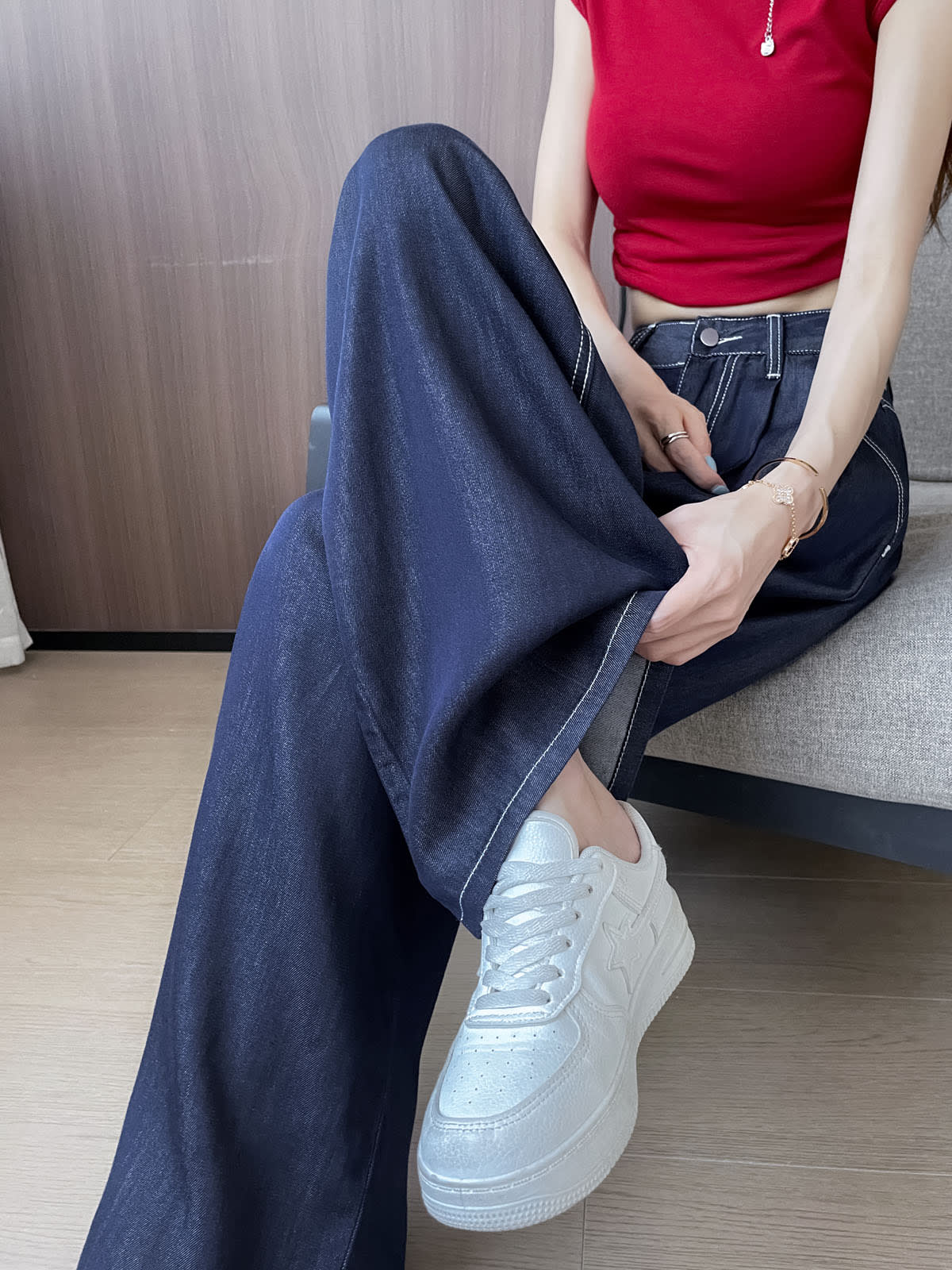 YEEYEEWang 데님 블루 와이드 레그 진, 아시안핏, 허리 아래 소파 앉은 포즈, 한 손으로 밑단을 들어 올린 모습, 화이트 스니커즈 매치.